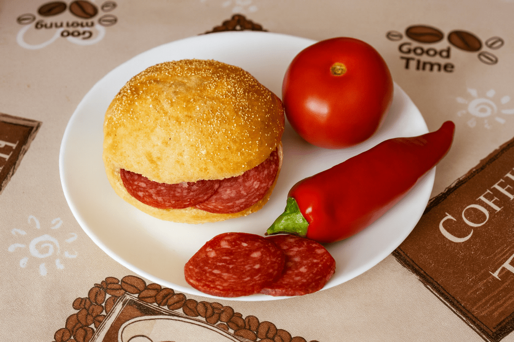 Fehér tányéron friss, ropogós zsemle szalámival, paprika és paradicsom társaságában - az osztás utáni egyszerű, de szeretettel teli pillanat emléke.